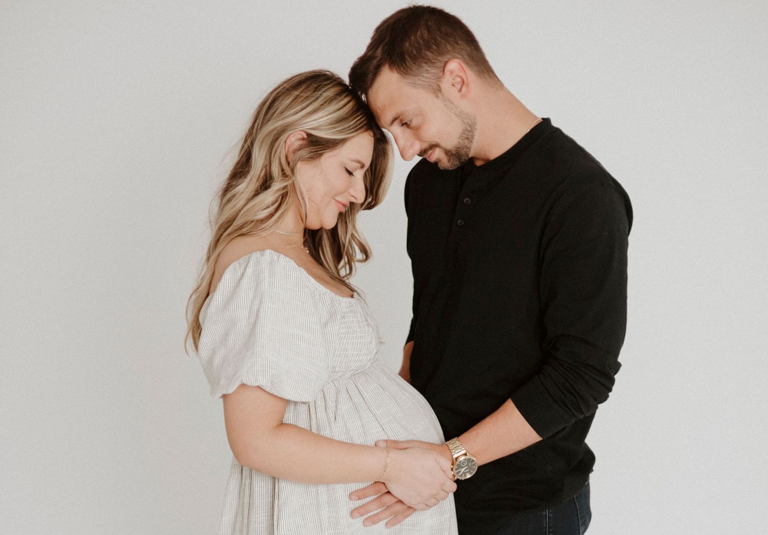 Maternity photo of couple in black and white clothing embracing against neutral backdrop.