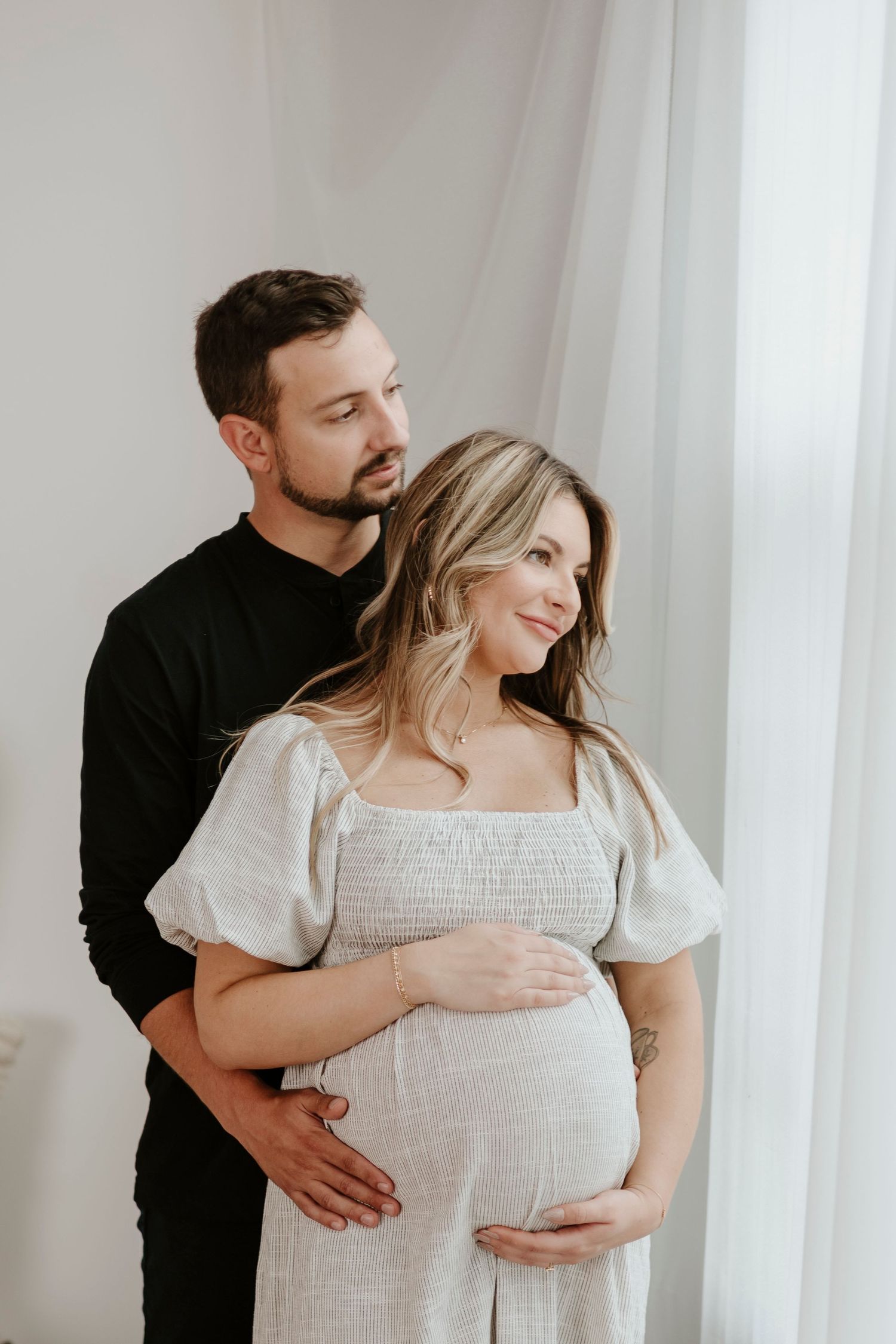 Intimate maternity portrait by window with couple in contrasting black and white outfits.