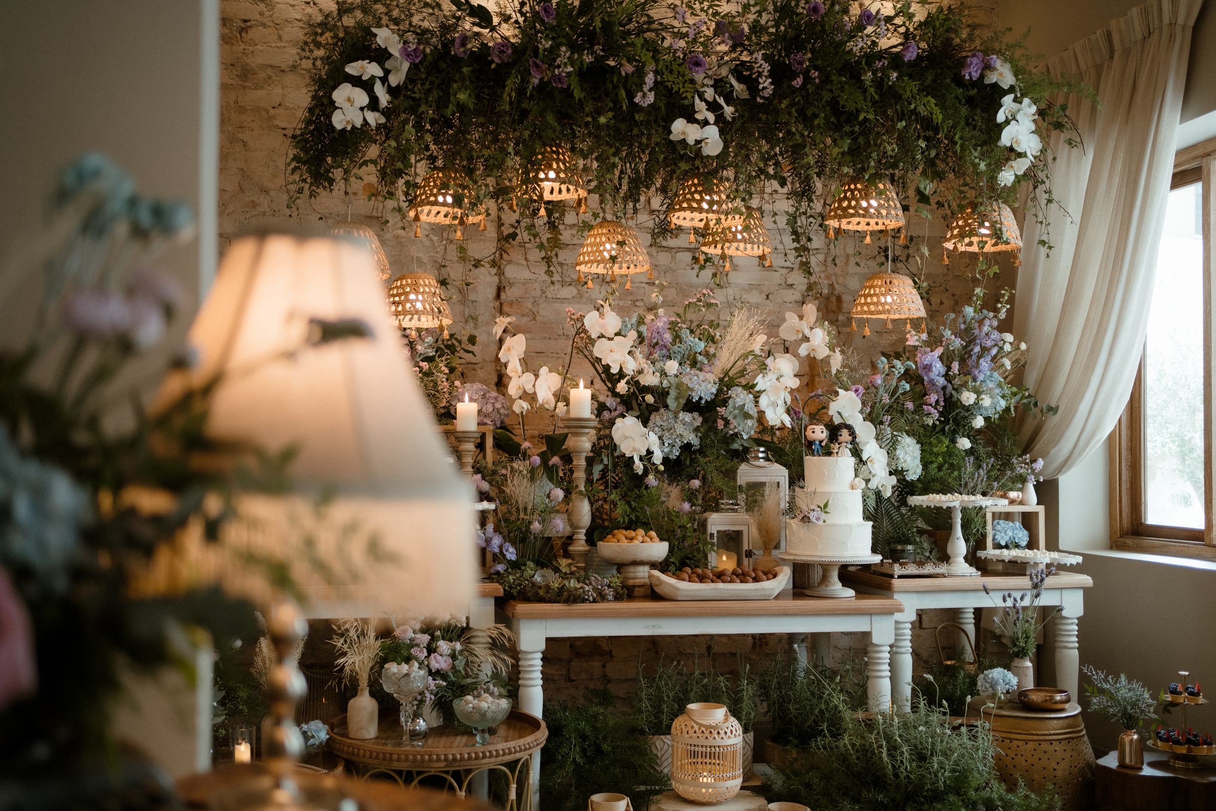Romantic wedding dessert display with white flowers and greenery against a rustic stone wall.
