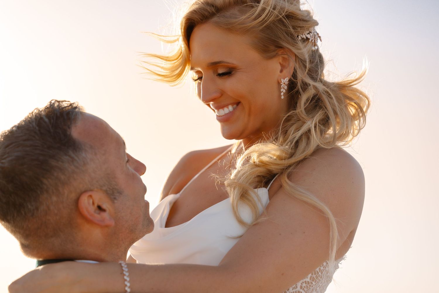 Bride smiling down at groom in golden sunset light during romantic outdoor wedding portrait.