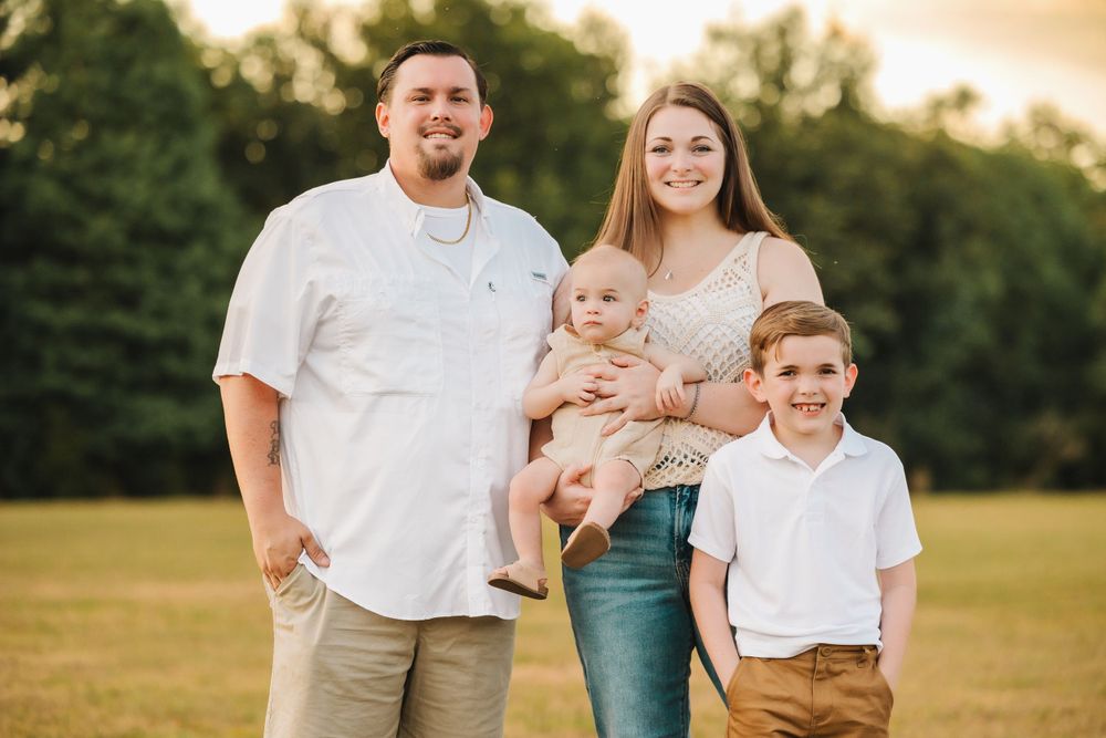 Young family of four smiling together in a golden hour outdoor field portrait.