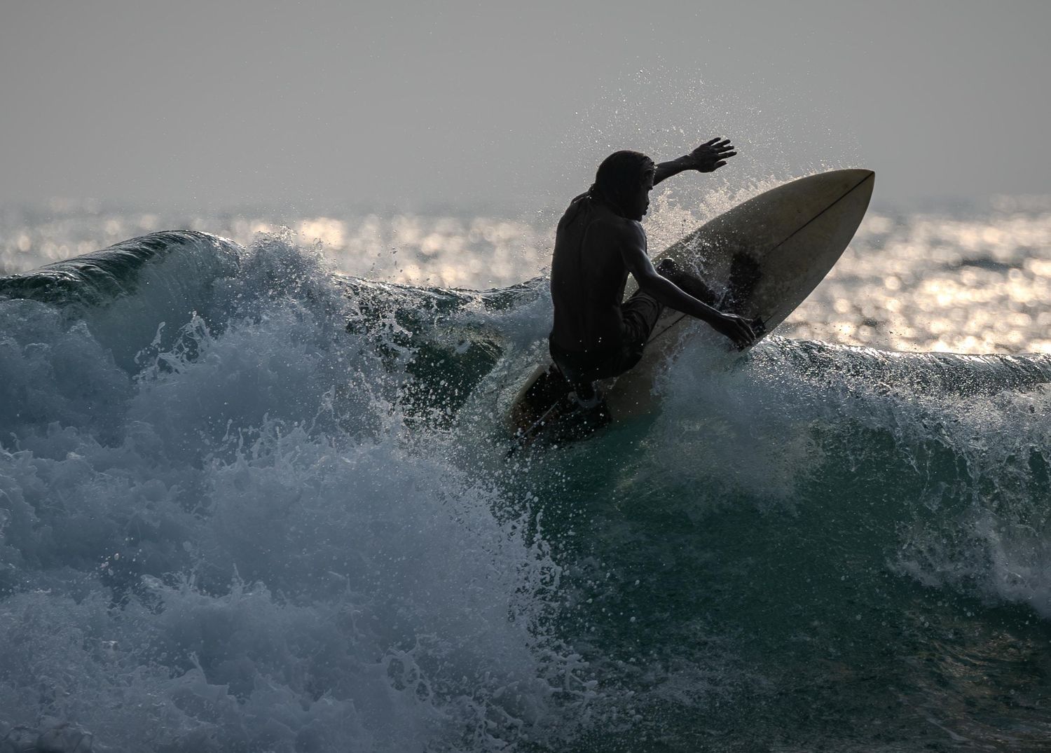 Surfer riding a large wave during sunset with dramatic ocean spray.