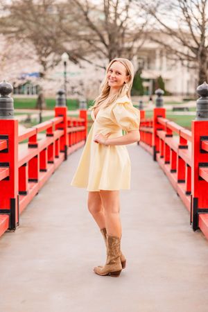 A senior girl posing on a red bridge and smiling with her hand on her hip in Downtown Huntsville Alabama