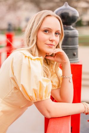 A senior girl smiling and leaning onto the red railing of a bridge in Big Spring Park