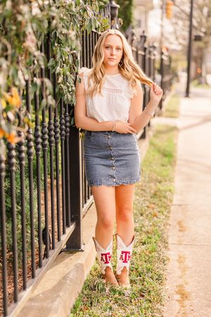 Person in white top and denim skirt posing against iron fence wearing university-themed boots.