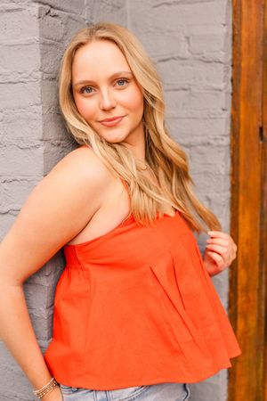 Senior girl in coral tank top posing against gray brick wall with wavy hair.