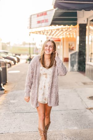 Casual portrait of woman in cardigan and boots laughing on downtown sidewalk.
