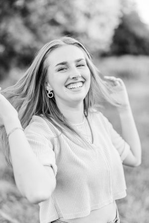 Black and white portrait of a joyful woman with blonde hair smiling outdoors.