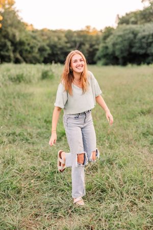 Woman in light colored clothing walking through tall grass in a natural outdoor setting.