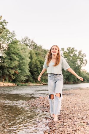 Woman in ripped jeans standing at water's edge in natural outdoor setting.