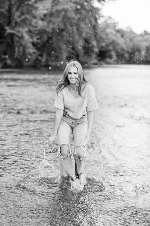 Black and white photo of person splashing in shallow water surrounded by nature.