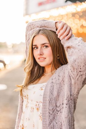 Portrait of woman in knit cardigan and floral dress with bokeh lights in background.