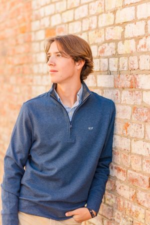 Casual portrait of young man in navy quarter-zip sweater against brick wall.