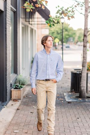 Young man in business casual attire walking down urban sidewalk.