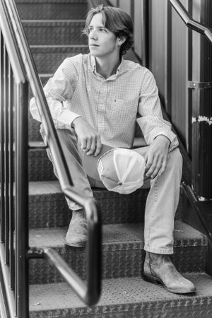 Young man in casual attire sitting on metal stairs with hat in monochrome.