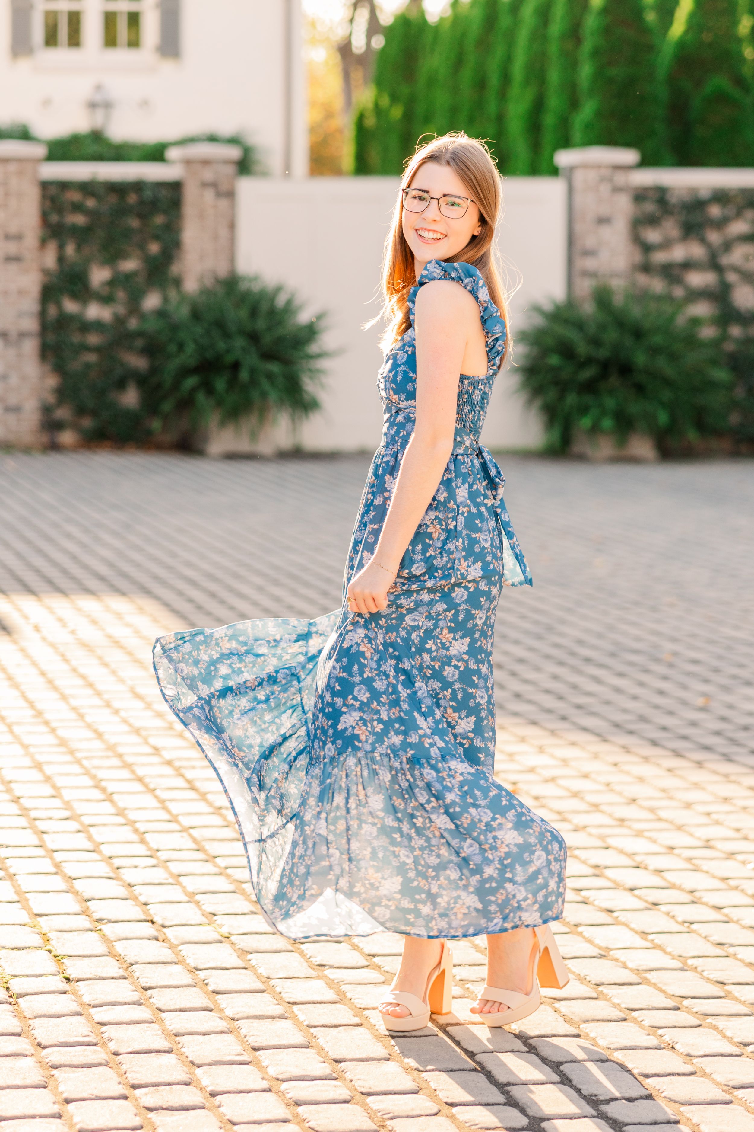 Woman in flowing blue floral dress twirling on cobblestone patio.