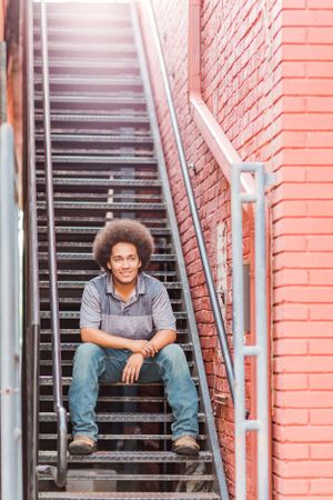 Portrait on metal stairs against red brick wall showing casual style and natural hair.