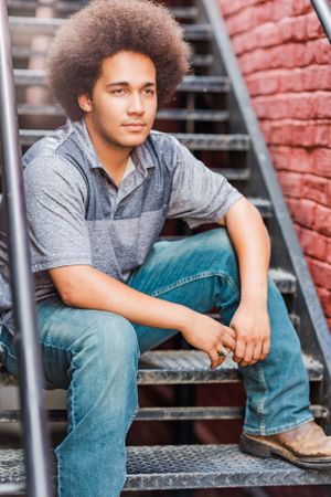 Casual portrait on metal staircase showing relaxed pose and natural hairstyle.