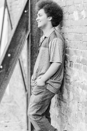 Black and white photo of someone with an afro hairstyle leaning against a brick wall.