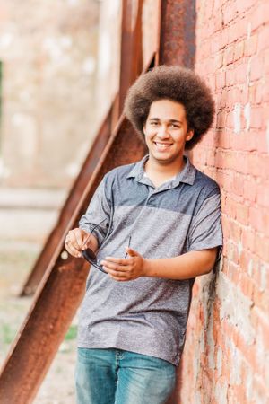 Casual portrait against a brick wall showing a natural afro hairstyle and grey polo shirt.