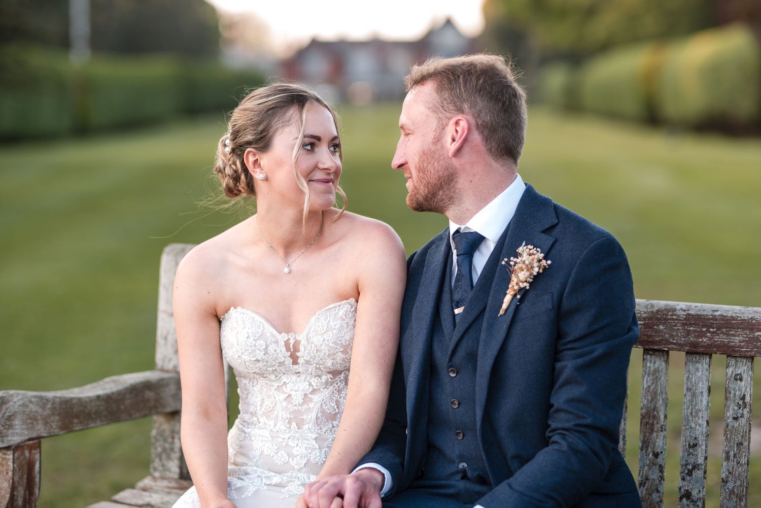 A couple shares an intimate moment while sitting on a wooden bench in a garden setting.