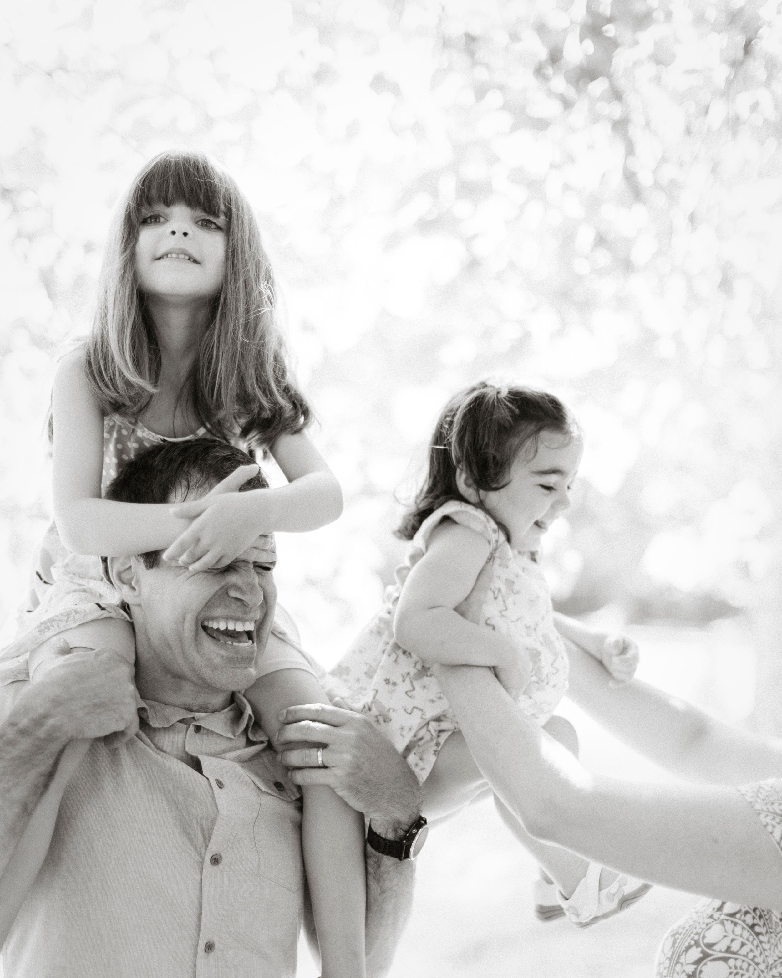 Black and white capture of playful outdoor family interactions with natural backlighting.