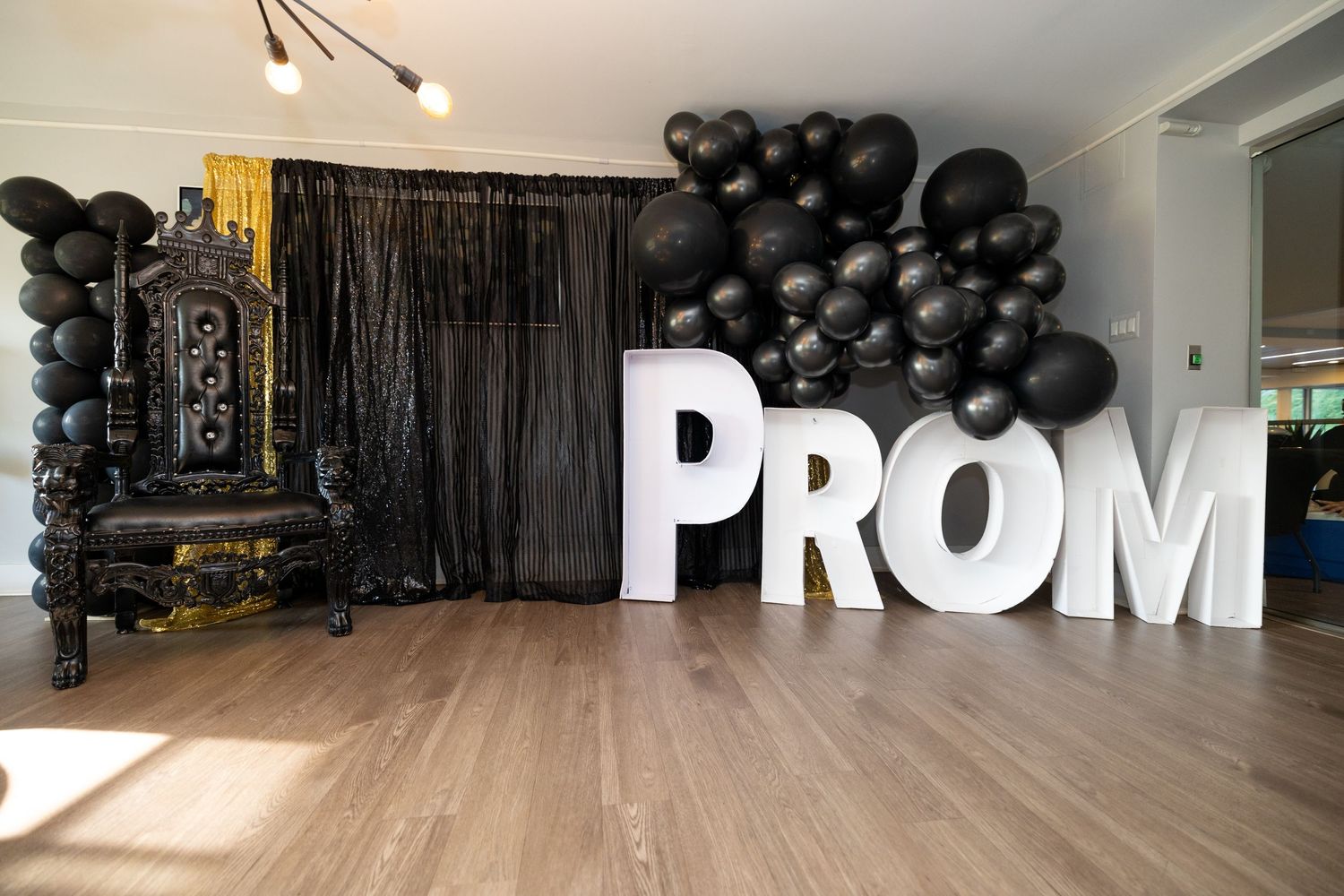 Modern prom photo setup with large white PROM letters and black balloon arch against dark backdrop.
