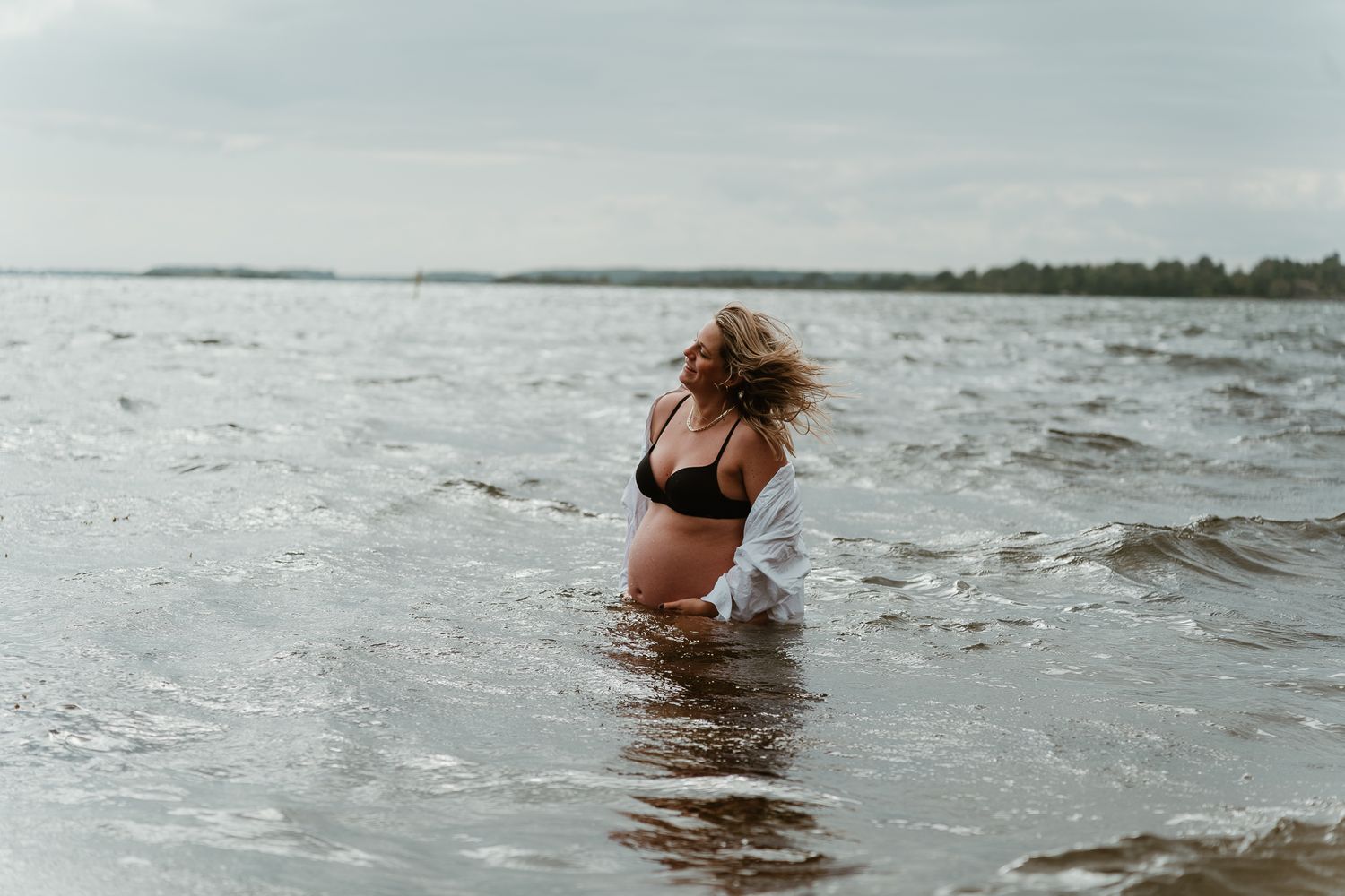 A woman wades through choppy waters at the beach on an overcast day.