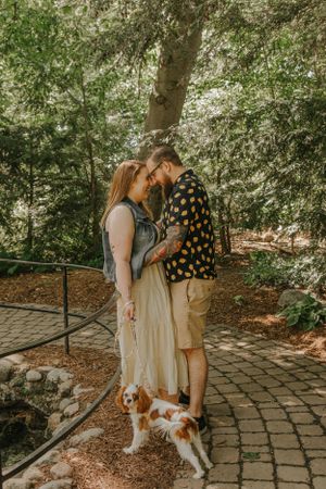 A couple and their dog enjoy a stroll through a wooded park area with stone pathways.