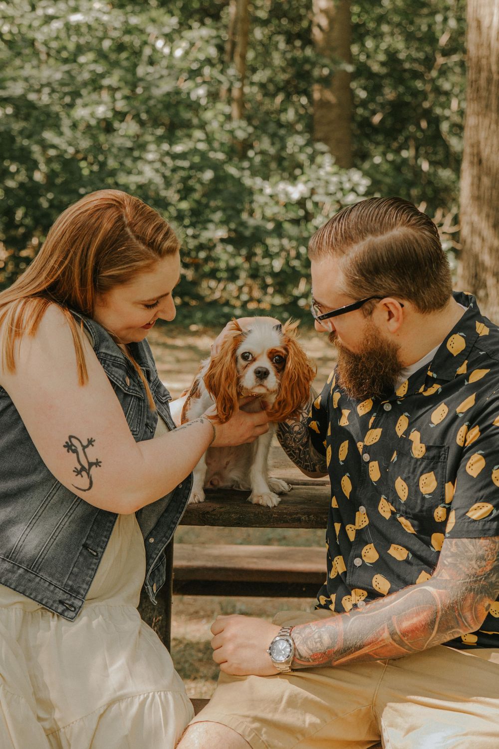 A couple and their Cavalier King Charles Spaniel dog enjoy a tender moment outdoors.