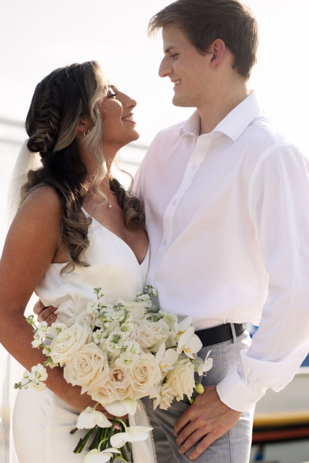 A romantic moment between a couple holding white roses against a marina backdrop.
