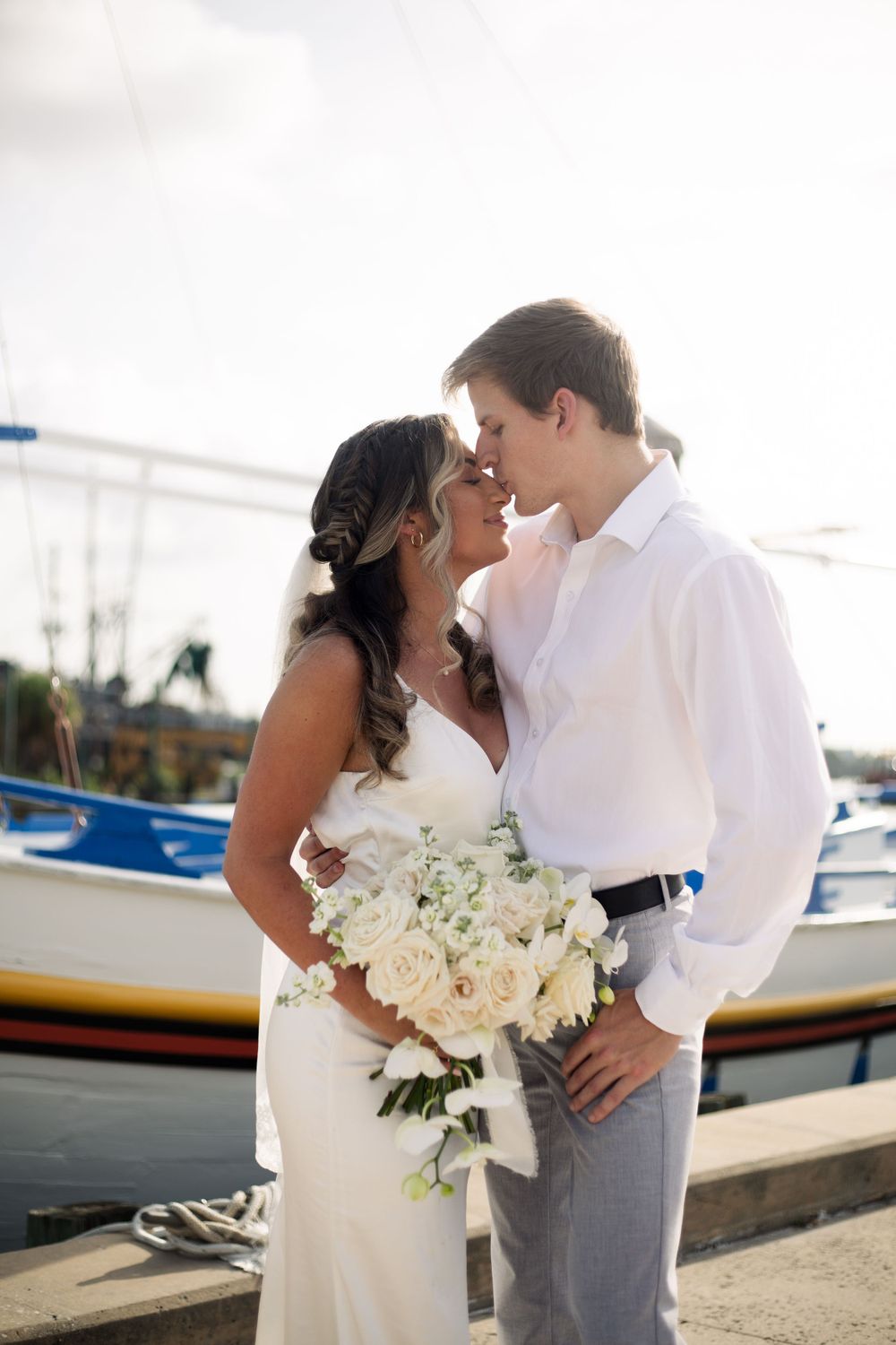 A tender wedding moment captured at a marina with boats in the background.