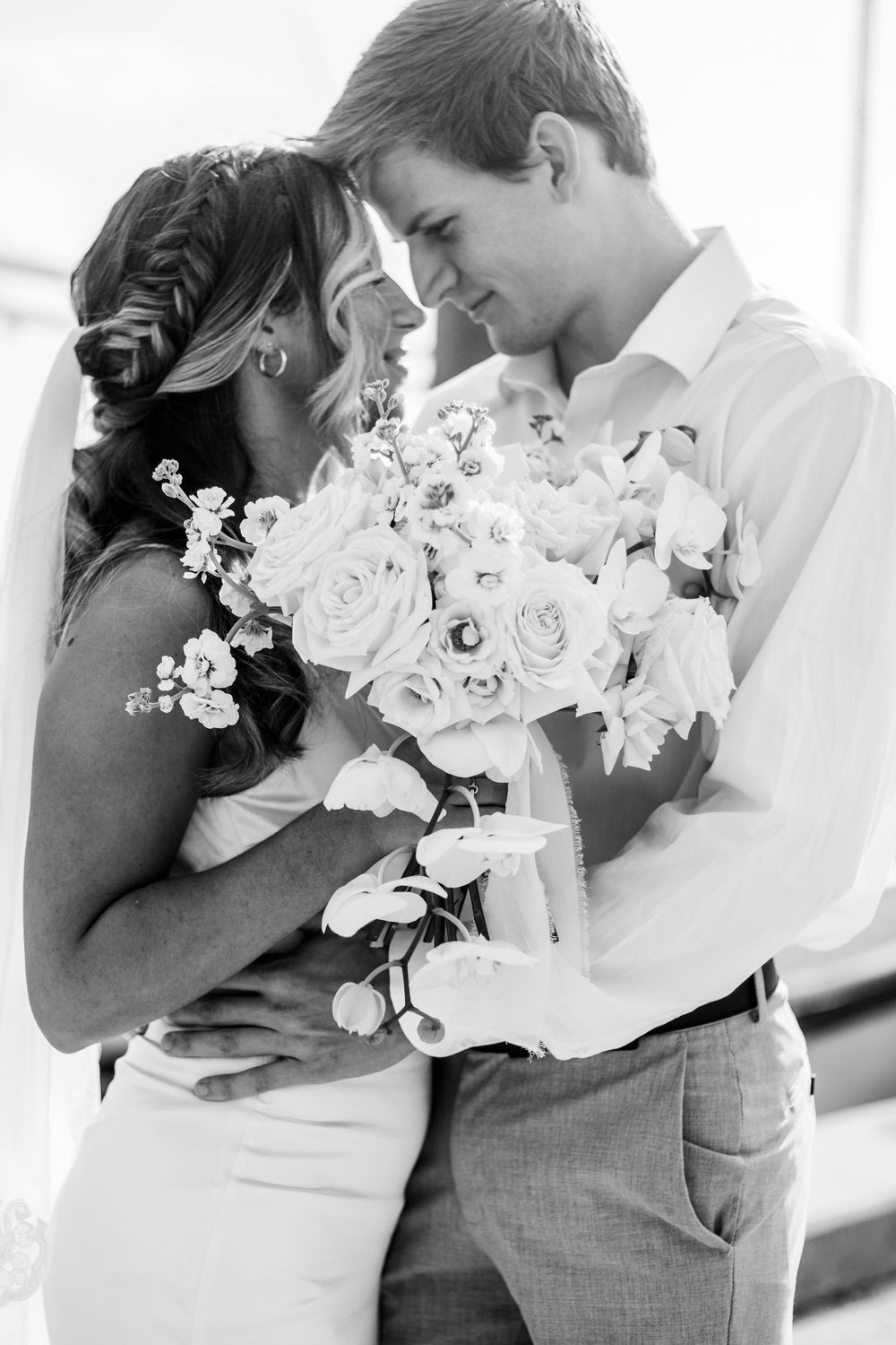 An intimate black and white portrait of a couple sharing a tender moment with white roses.