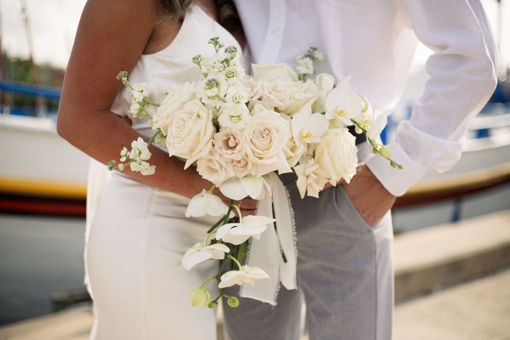 A close-up of white roses and orchids in a wedding bouquet against formal attire.