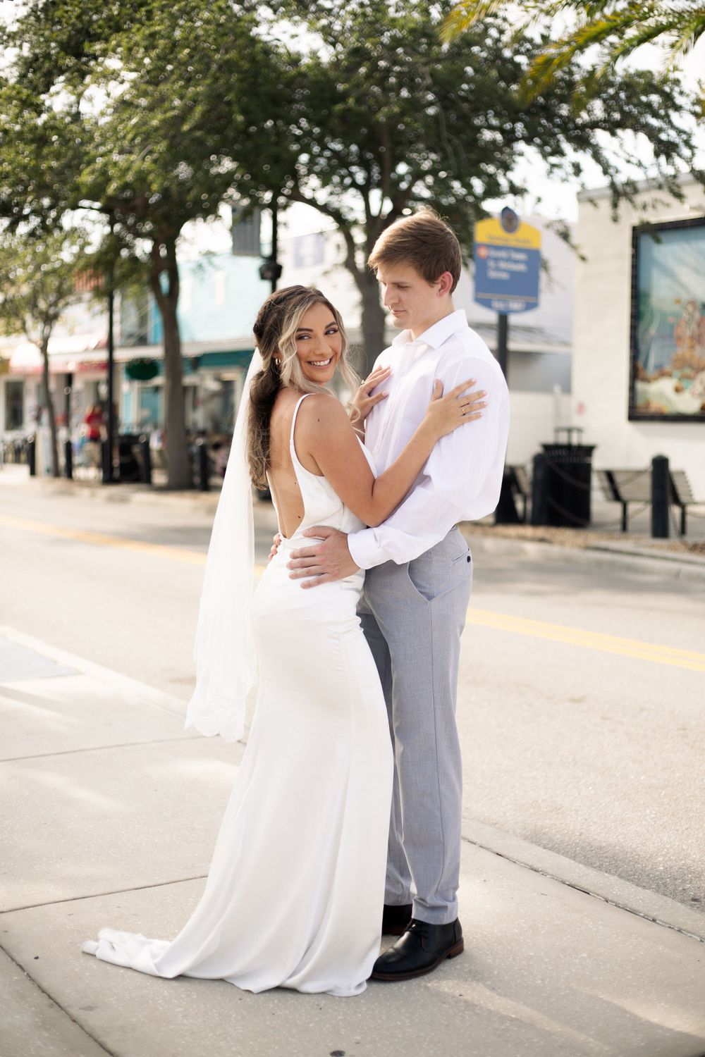 Wedding couple embraces on a palm-lined street during their special day.