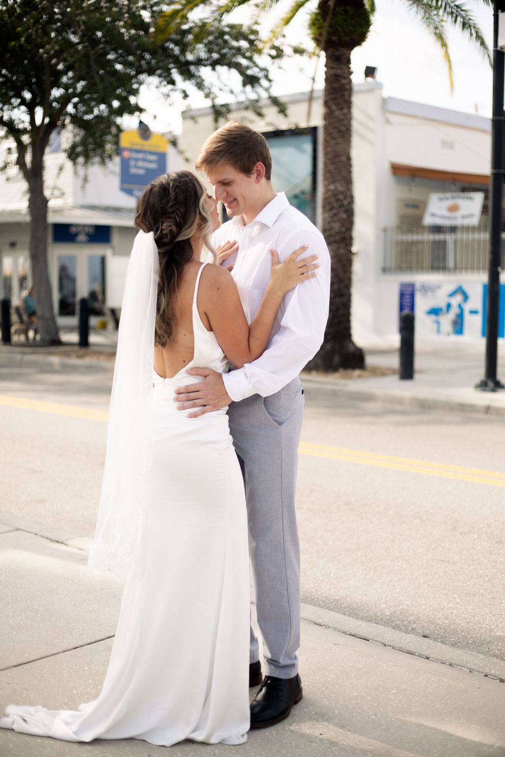 Romantic embrace between newlyweds on a sunny urban street with palm trees.