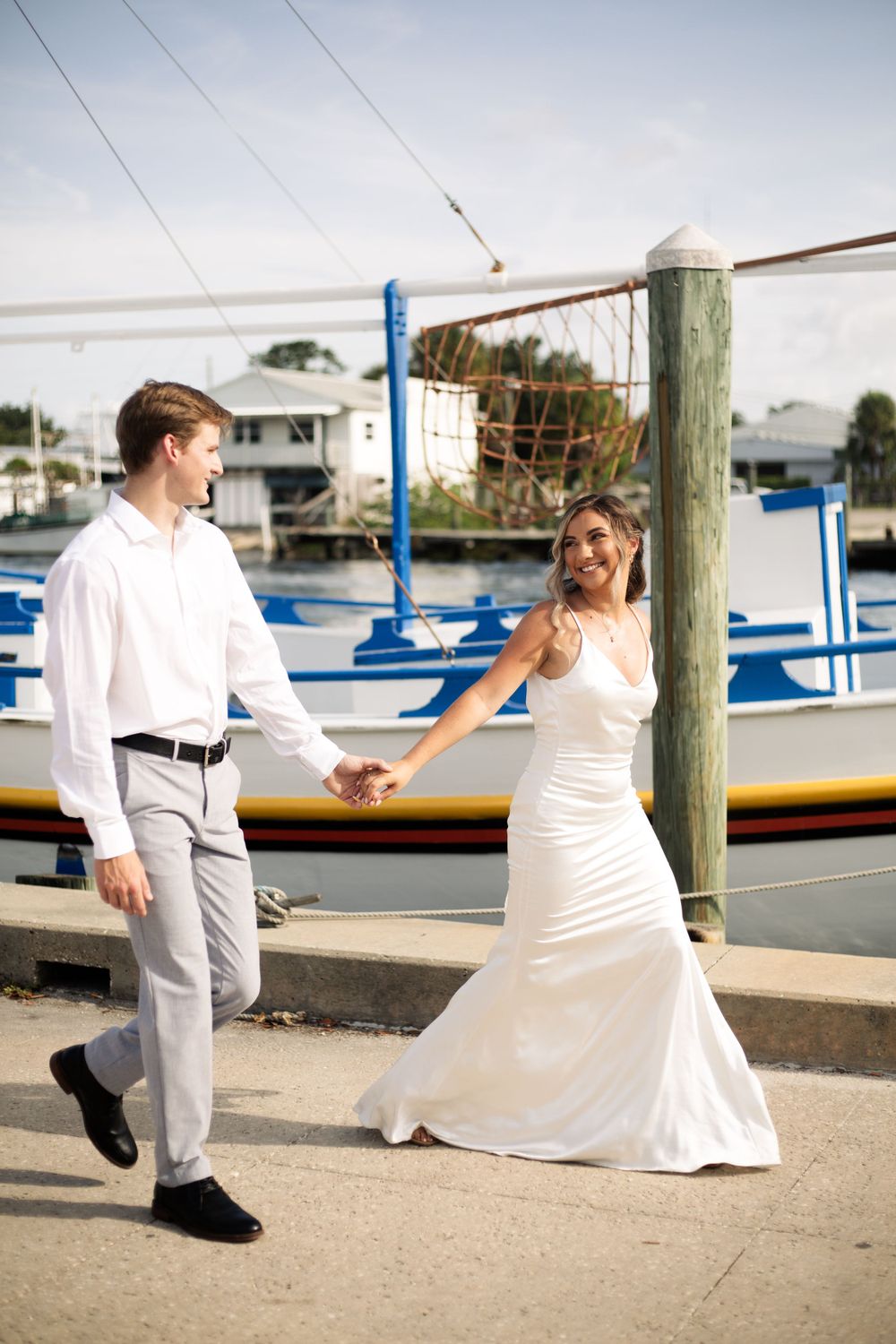 Wedding couple dances playfully on a marina dock with boats in background.