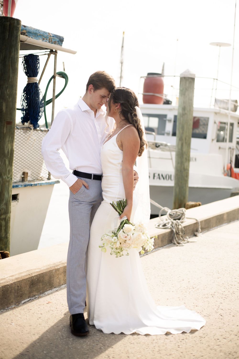 Romantic wedding portrait of couple standing by marina with boats in background.