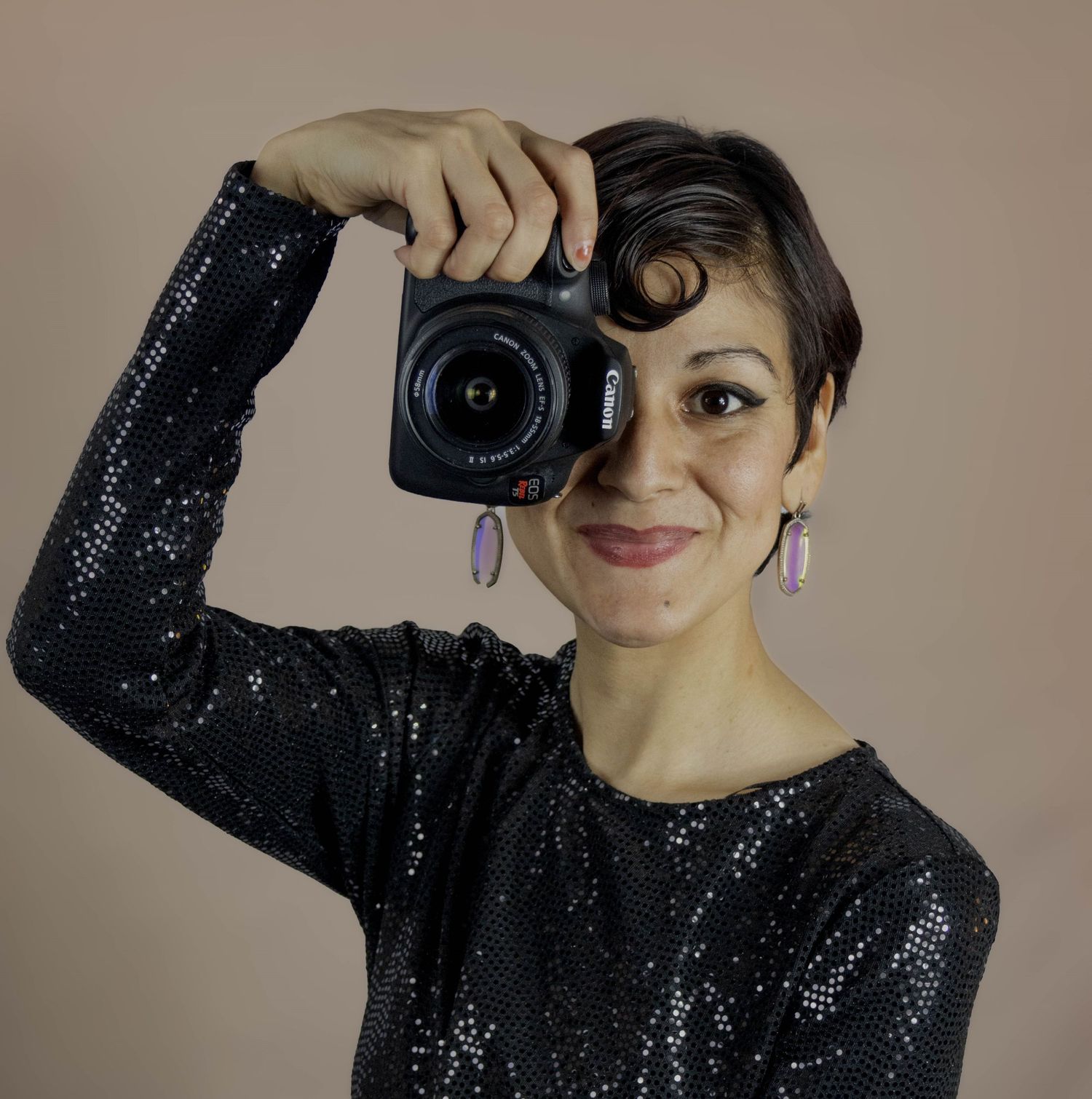 female photographer wearing sequined dress and holding digital camera over one eye
