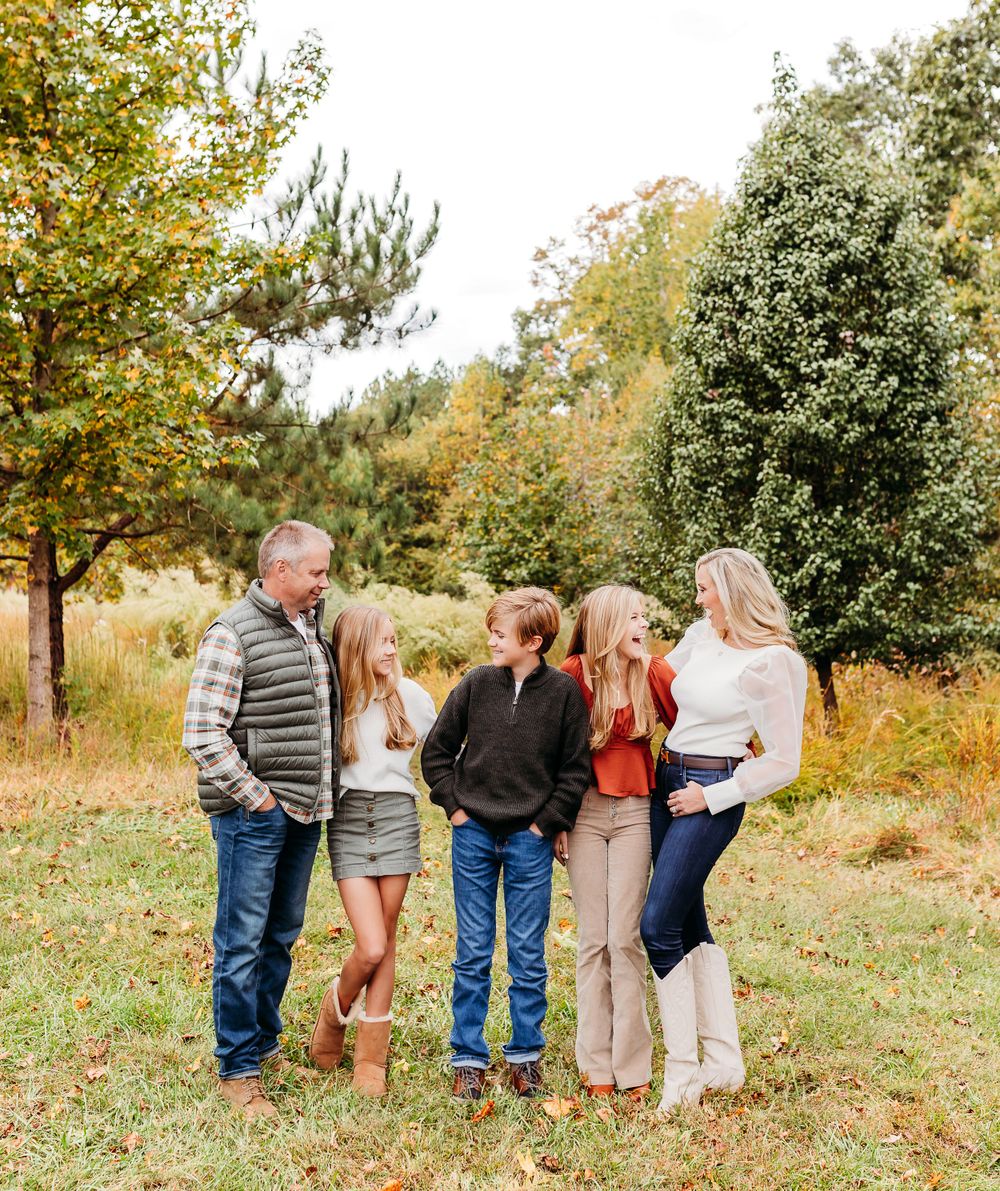 A group of people walking together through a grassy field on an autumn day with trees in the background.