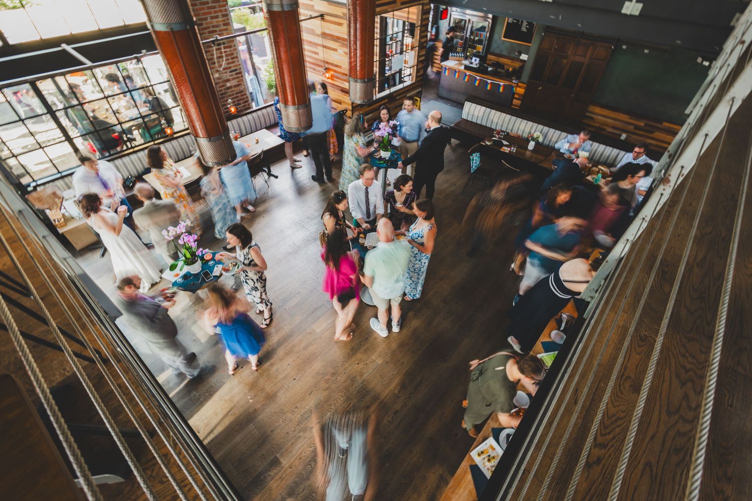 Aerial view of wedding reception with guests mingling on wooden dance floor.
