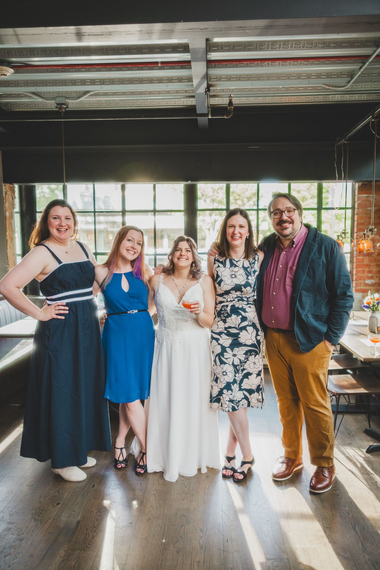 Small group poses together at wedding celebration in industrial-style venue with natural lighting.