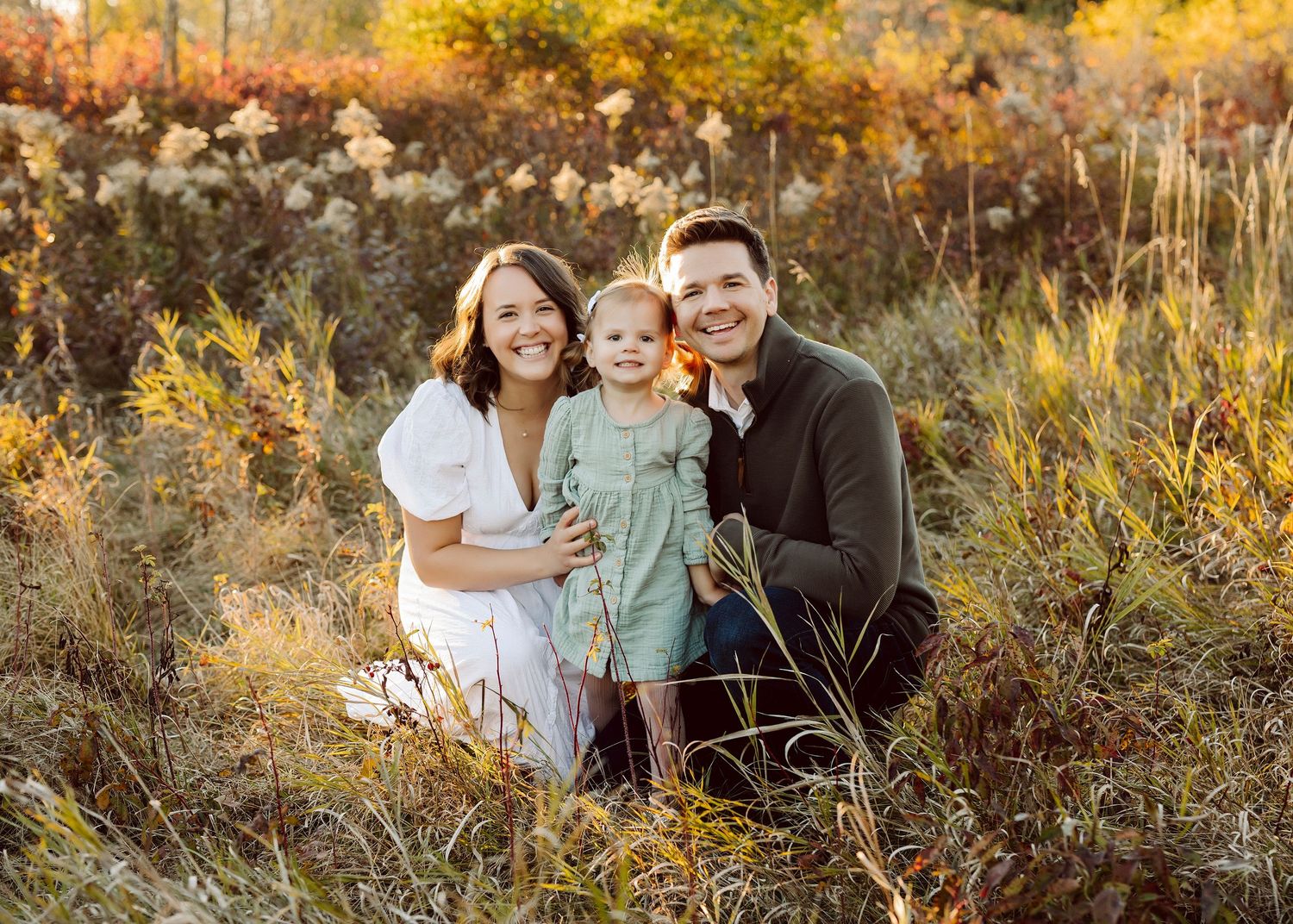 Family group embracing in golden autumn field during sunset photoshoot.