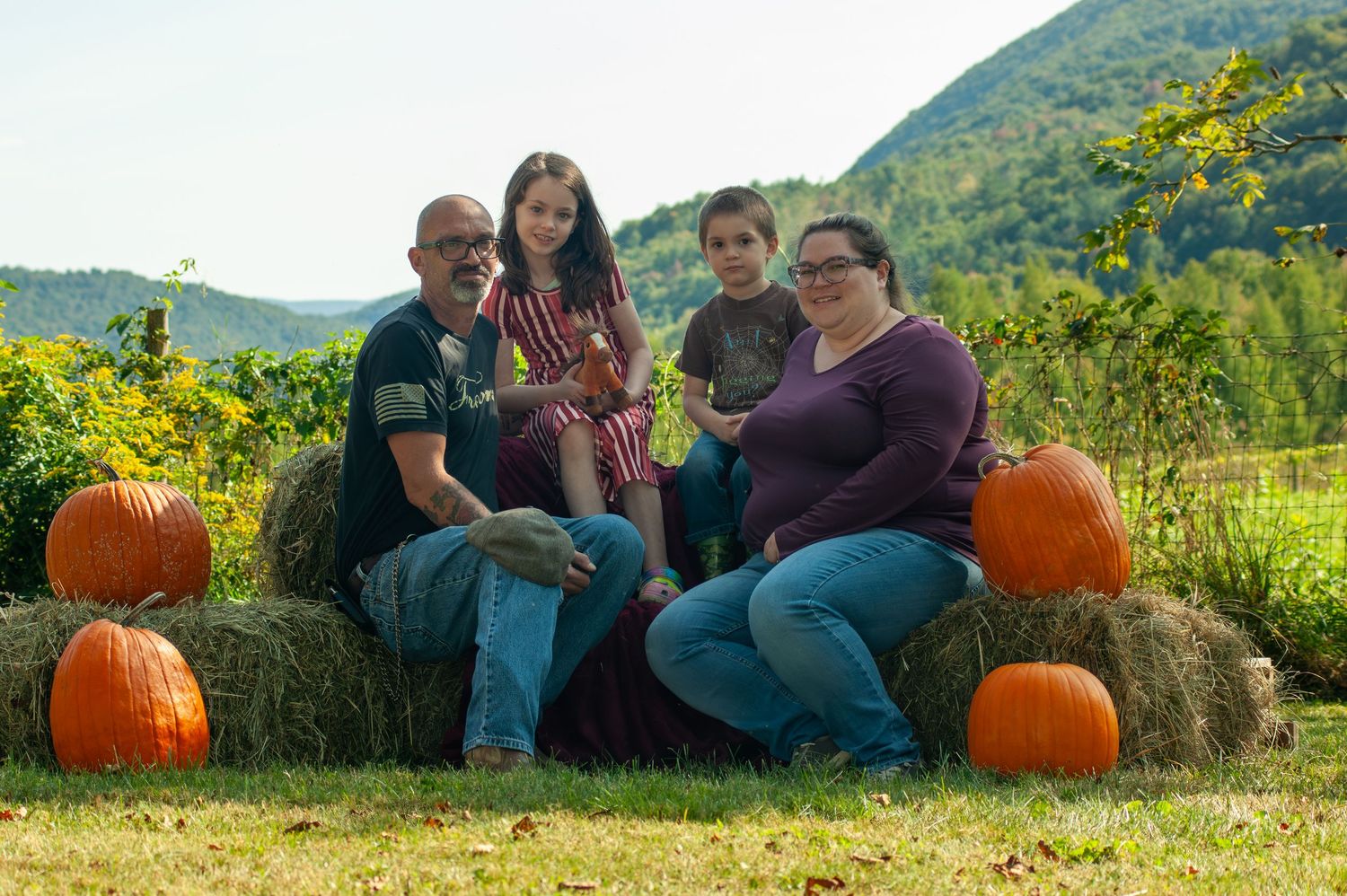 Group sitting on hay bales surrounded by autumn pumpkins with mountains in background.