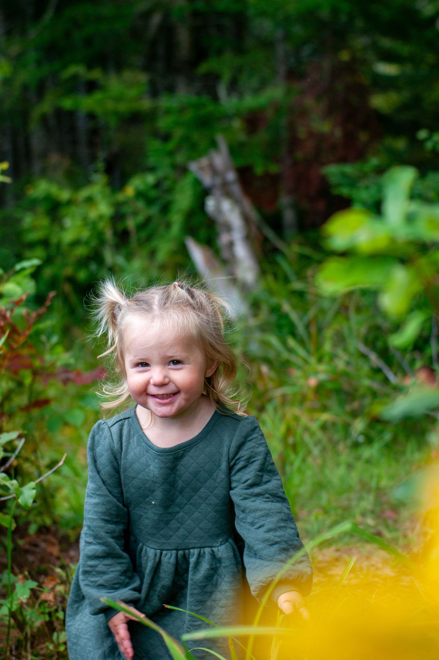 A child smiles playfully in a lush forest setting.