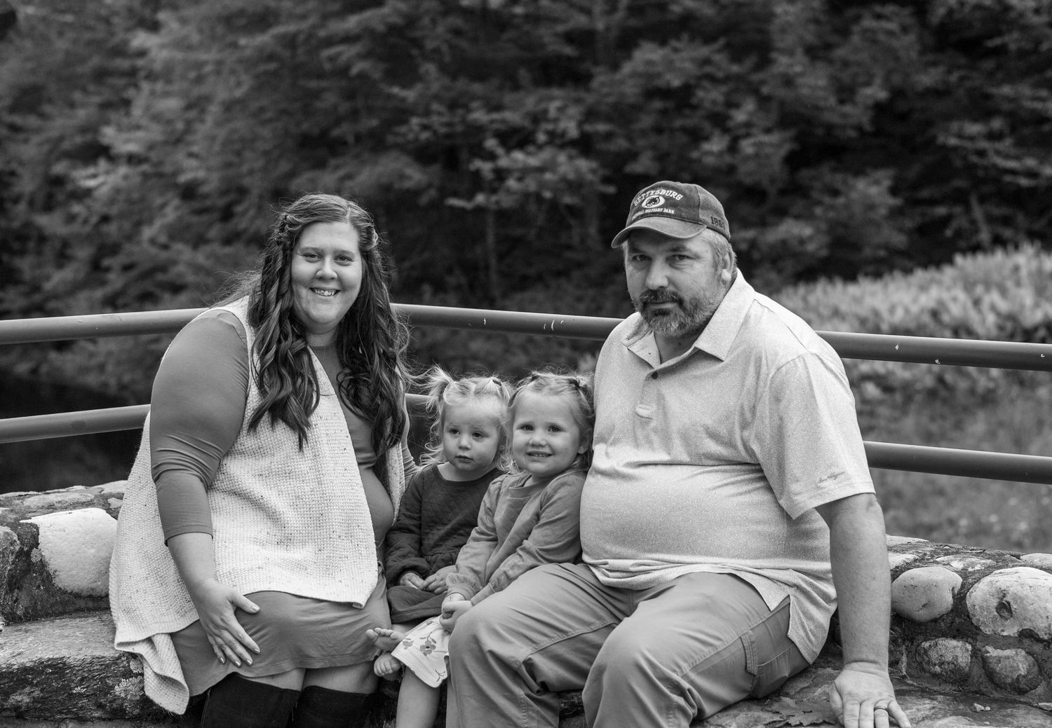 A family sits together on a rustic stone wall with forest scenery behind them.