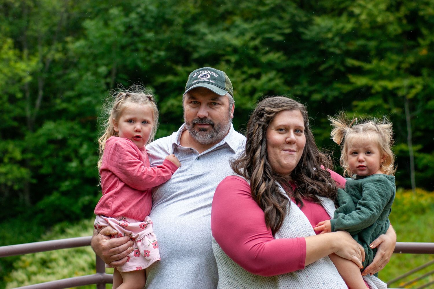 A family of four poses together on an outdoor walkway surrounded by green forest.
