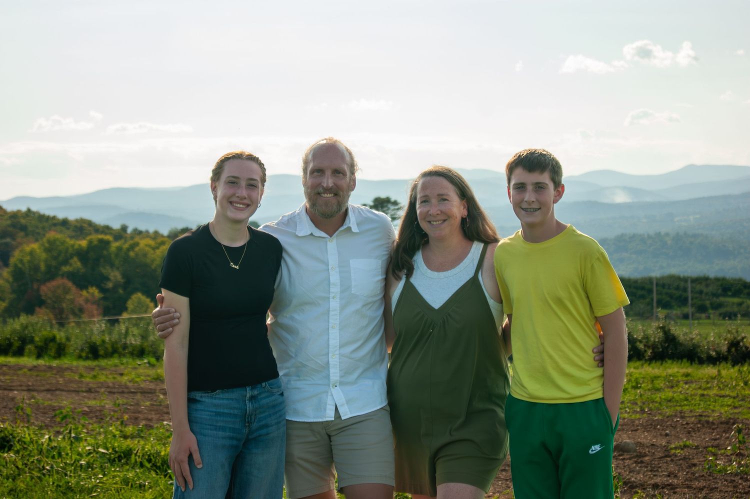A group of four people pose together on a hilltop with mountains in the background.
