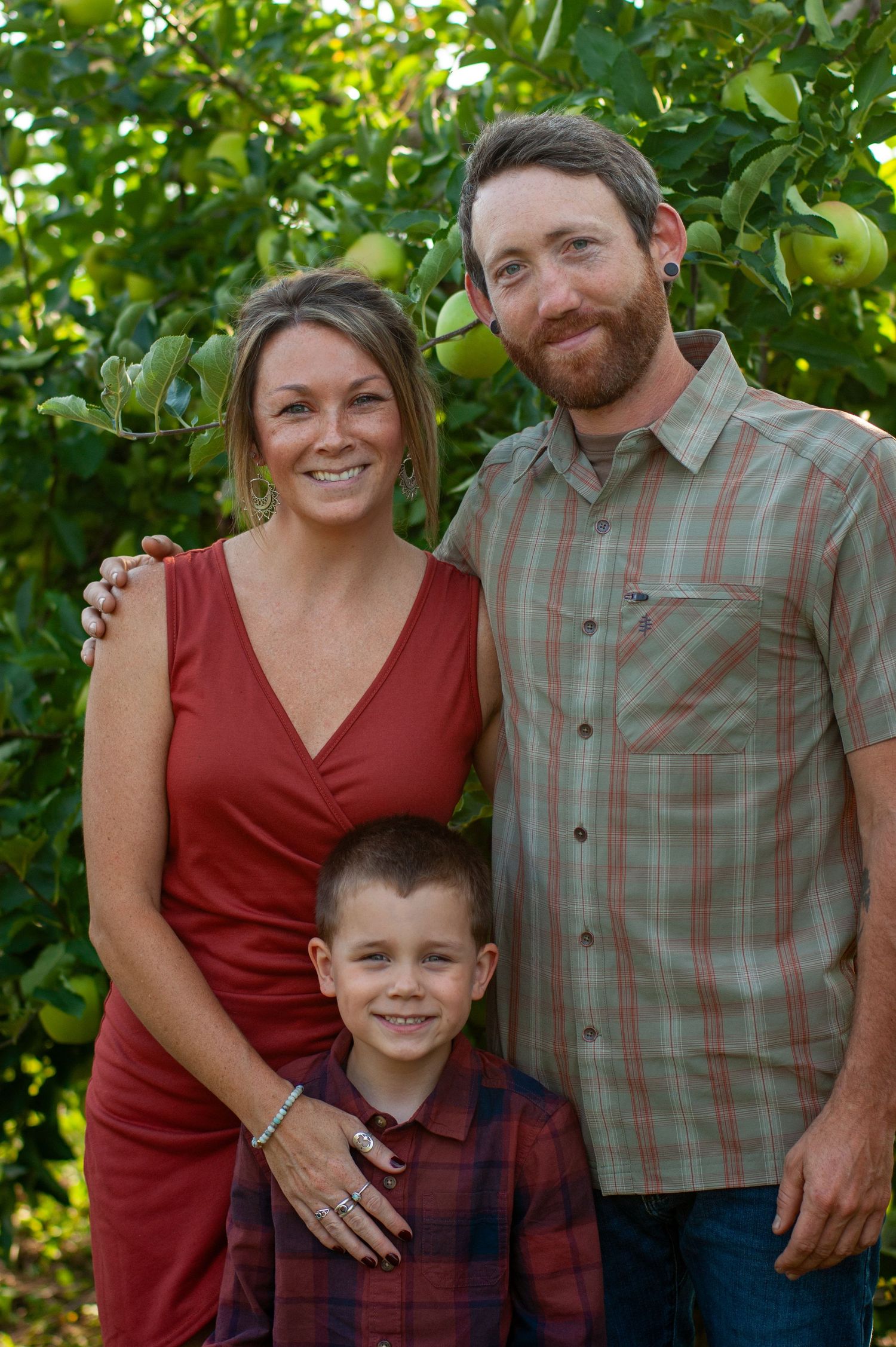 Family of three poses together among apple trees in an orchard.