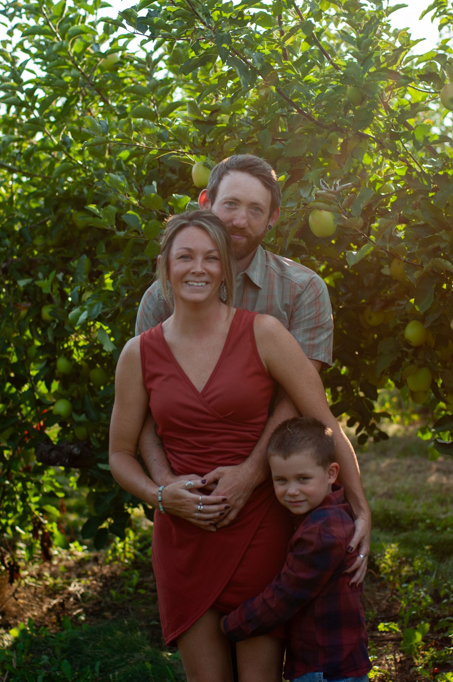 Family portrait with sunlight filtering through apple tree branches.